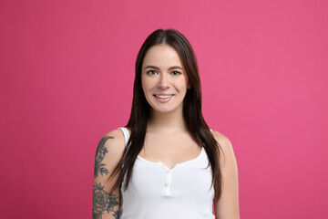 Fototapeta premium Beautiful woman with tattoos on arm against pink background