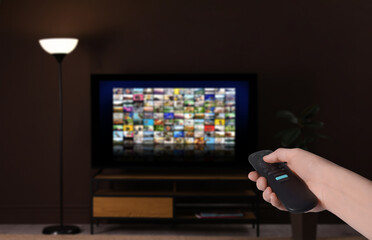 Fototapeta premium Woman with remote control changing channels while watching TV at home, closeup