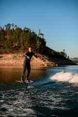 Athletic guy masterfully rides on river water on a foil wakeboard on beautiful landscape background.