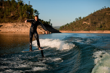 active man skilfully rides on river water on a foil wakeboard on beautiful landscape background.