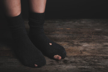 Poor person in shabby socks on wooden floor, closeup
