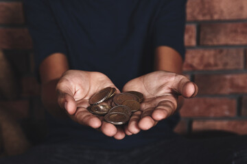 Poor homeless boy begging near brick wall, focus on hands