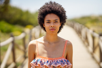 Young black woman, with afro hair, on a wooden path on the dunes of a tropical beach.