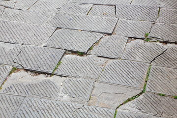Old and damaged carved paving made with chiseled grey sandstone blocks in a pedestrian zone