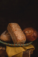 Homemade whole grain breads in a basket. Sesame bread and rye bread on a dark rustic background.