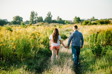 Rear view of a romantic man and woman walking on field grass, nature enjoying sunlight. Concept of lovely family holding hands. Young couple running and looking away. Back view.
