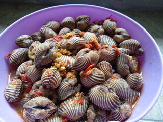  Boiled cockles,  blood clams seasoned with red onion, garlic and cayenne pepper. placed in a purple plastic bowl, top view of hot delicious sauce, Indonesian food