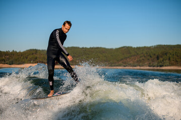 young active man on a wakesurf board balances on a wave