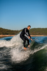 Active athletic man riding with wakesurf board on splashing river wave