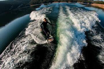 high angle view of young athletic man masterfully balancing on a wave on a wakesurf board