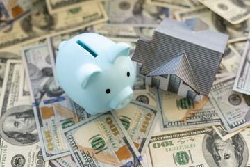 Small paper house and piggy bank on a pile of dollar banknotes, Money background