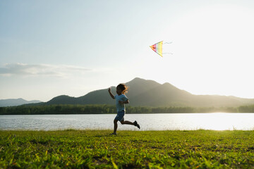Child playing with a kite while running on a meadow by the lake at sunset. Healthy summer activity for children. Funny time with family. - Powered by Adobe