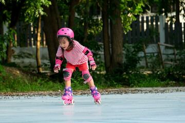 Cute Asian little girl in protective pads and safety helmet practicing roller skating in the park. Exciting outdoor activities for kids.