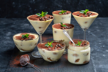 Traditional Italian dessert tiramisu decorated with cocoa powder, coffee beans and green mint on table, close up