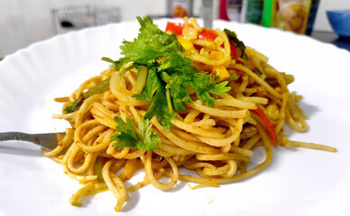 Homemade Indo-Chinese recipe Schezwan Noodles or vegetable Hakka Noodles or chow mein with Corn and tomato served in a white plate on wooden table. selective focus