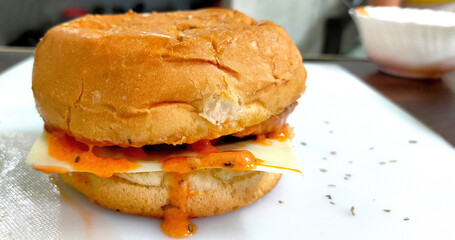 Close-up of delicious fresh home made burger with aloo tikki, cheese, onion and tomato on a white plate on wooden table background