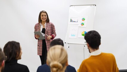 Business woman coach trainer presents a report, shows diagrams on flip chart in conference hall. Project manager reporing on presentation to employees in office. Female teacher leading a master class.