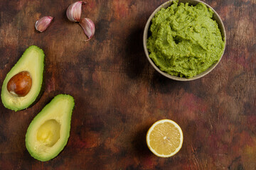 Traditional latinamerican mexican sauce guacamole in clay bowl, cut half avocado and avocado sandwiches on dark background. Top view