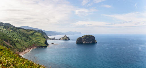 Wide panorama of emerald green cape cabo Machichaco of Basque coast and two small islands...