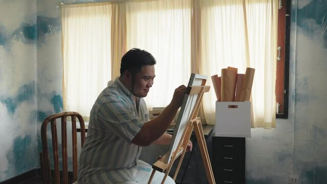 Portrait of a chubby Asian young man happy creating front of canvas