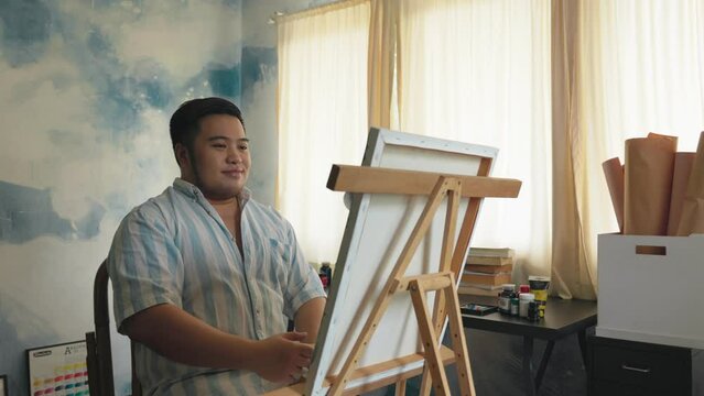 Portrait of a chubby Asian young man happy creating front of canvas