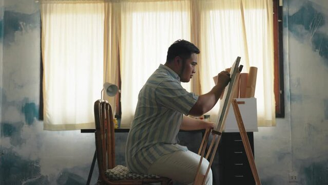 Portrait of a chubby Asian young man happy creating front of canvas