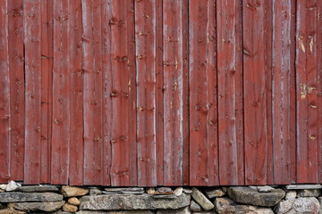 Facade of a Scandinavian type wooden building with red wooden boards where the lower part is a stone wall under which there is dry grass