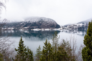 Norwegian fjord with clear water in early spring when there is still some white snow in the mountains and they are foggy