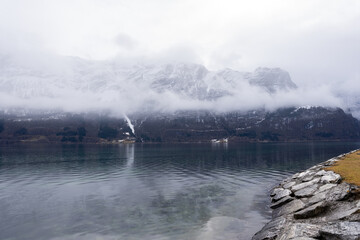Norwegian fjord with clear water in early spring when there is still some white snow in the mountains and they are foggy