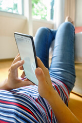 Closeup of woman lying on floor and using smartphone at home