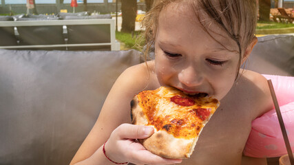 A little girl is happy to eat pizza in a beach cafe.