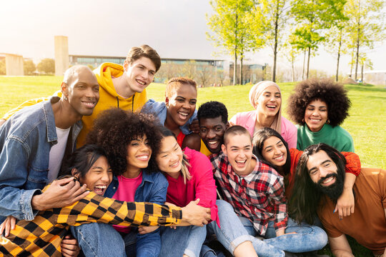 Large group of cheerful young multiracial friends having fun in park outdoors. Happy people looking at camera, community, youth lifestyle and travel friendship.