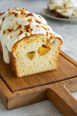 Pound cake with peaches, cream glaze and caramel on a wooden board against a concrete background. Close-up