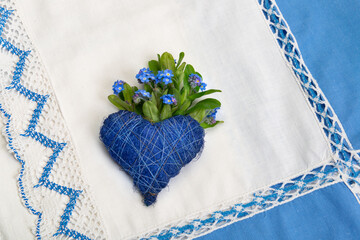 Blaues Herz auf einer alten Tischdecke mit Stickbordüre