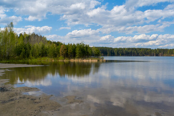 Scenic view at beautiful spring day on a forest lake. Deep blue cloudy sky and forest on a background, spring landscape.