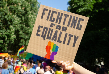 Woman holding placard sign Fighting for Equality with rainbow flag fist, during LGBT Pride Parade....