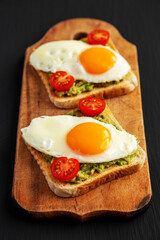 Homemade Healthy Egg, Avocado and Tomato Toast on a rustic wooden board, side view. Close-up.