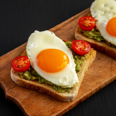 Homemade Healthy Egg, Avocado and Tomato Toast on a rustic wooden board, side view. Close-up.