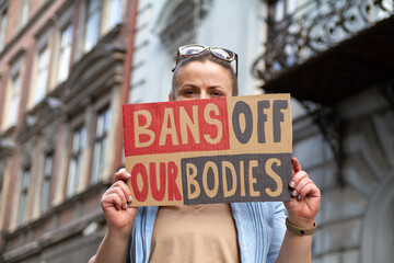Woman holding sign with slogan Bans Off Our Bodies. Protester with placard supporting abortion rights at protest rally demonstration. - obrazy, fototapety, plakaty