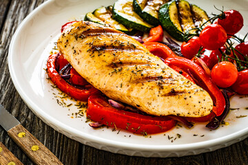 Grilled chicken breast with pepper, zucchini and cherry tomatoes on wooden table
