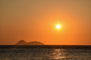 Naklejka na ściany i meble Orange sunset on Matala hippy beach with view on Paximadia islands in Crete, Greece