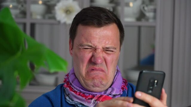 Annoyed millennial man with disgust look at smartphone screen at modern kitchen. Portrait of manager cringe and looking at phone screen with squeamishness, bad joke or inappropriate content.