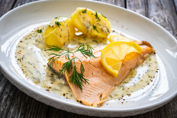 Roasted trout fillet with potatoes and dill sauce served on wooden table
