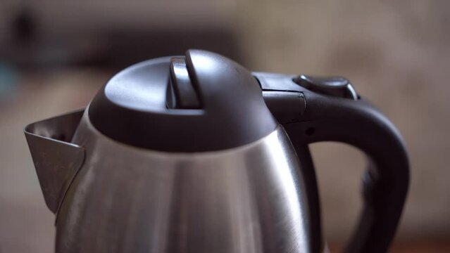 Button for turning on the electric kettle for boiling water. An electric kettle boils water. Person turns on the electric kettle.