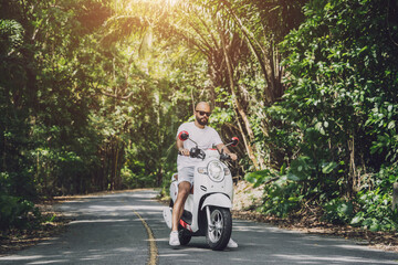 Stylish young man and his motorbike on the road in the jungle