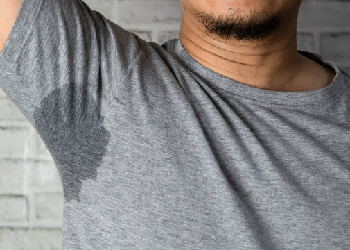 Sweaty man with stain wet armpit on t-shirt against gray