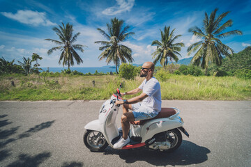 Fototapeta na wymiar Stylish young man rides a motorbike on the road near the sea and palm trees