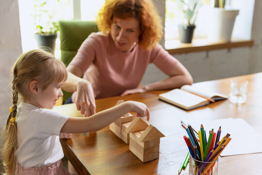 Smiling woman and cute little girl, mother and daughter playing with wooden toy cubes at home. Concept of family, support, studying, childhood, emotions