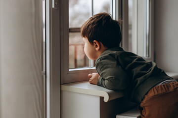 Fototapeta na wymiar Little, pensive, two years old boy sitting by the window and playing with toy children's car