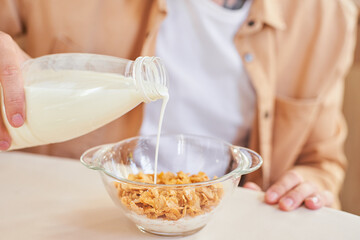 Close-up, a man pours milk into cereal.